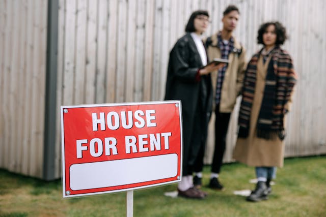 three-people-standing-behind-for-rent-sign